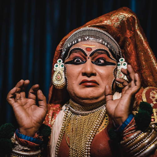 Kathakali actors in elaborate costume and makeup performing on stage with vibrant expressions.