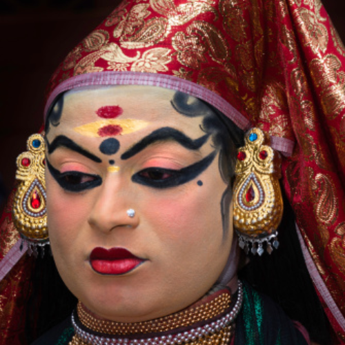 Kathakali actors in elaborate costume and makeup performing on stage with vibrant expressions.