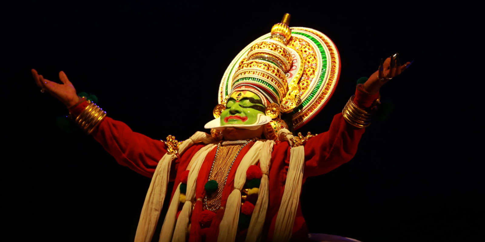 Kathakali dancer performing on stage with intricate makeup and costumes.