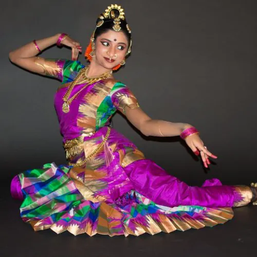 Young Kuchipudi dancer in vibrant costume performing traditional Indian dance move with expressive gestures.