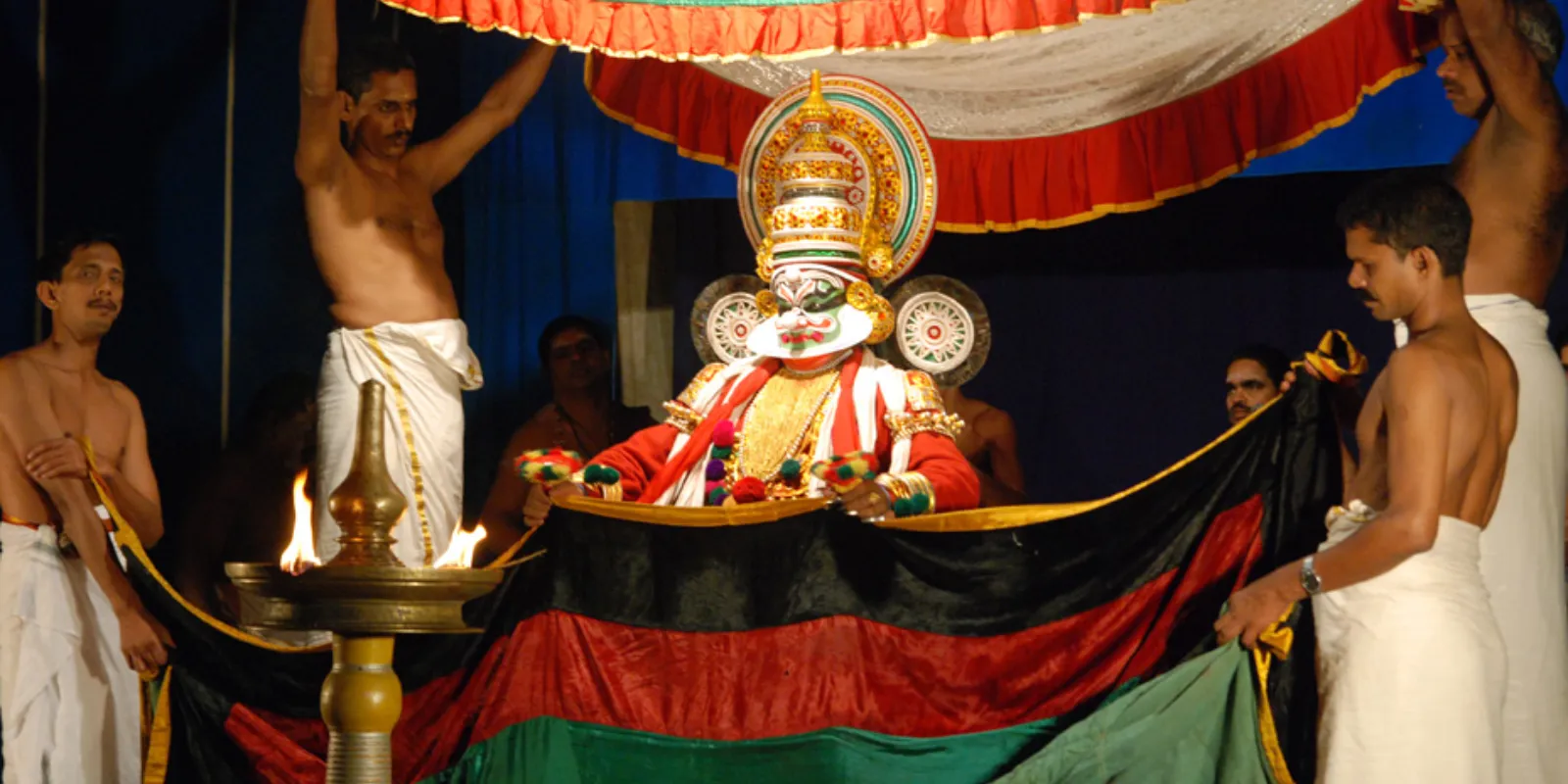 Kathakali stage adorned with vibrant backdrops and lighting, featuring a performer in traditional costume.